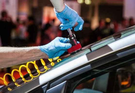 A person in blue gloves using a tool to repair a car's windshield