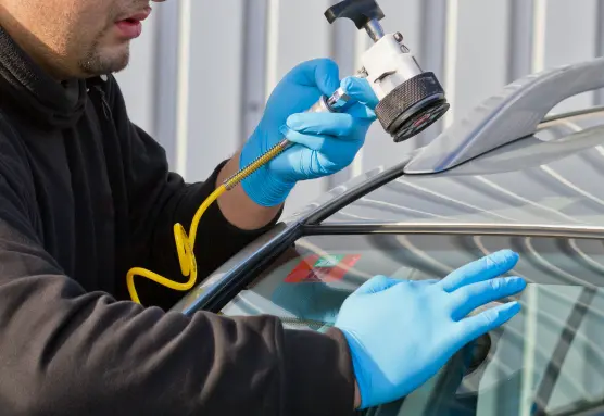 a person wearing gloves and holding a tool to repair a windshield