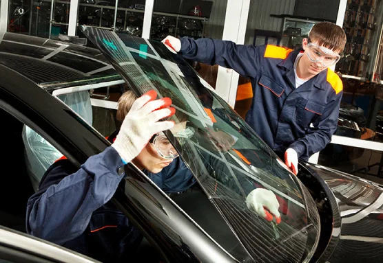 A group of men in blue uniforms are working on a car, replacing its windshield.