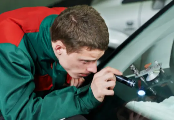 A person in a green and red uniform is repairing the car's window glass by using some tool.