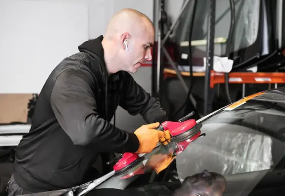 A person in a black hoodie is replacing the windshield of the car by using the suction cup.