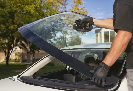 A person wearing black gloves holding the rear windshield of a white car with the help of a suction cup