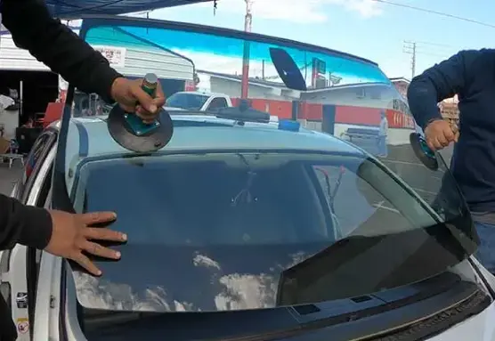 Group of men holding the front windshield of a white car with the help of a suction cup