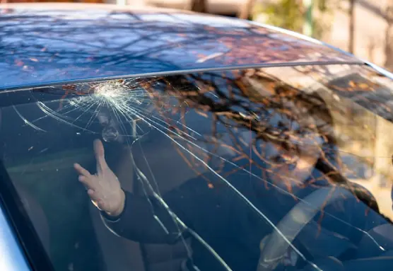 A woman is sitting in a car having a broken windshield.