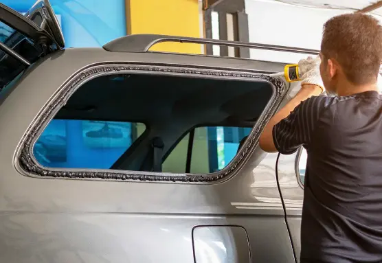 A person is using a caulking gun to seal the rear window of the car