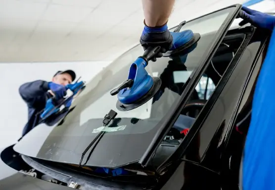 Group of men wearing gloves holding the rear windshield of a car with suction cups to replace it