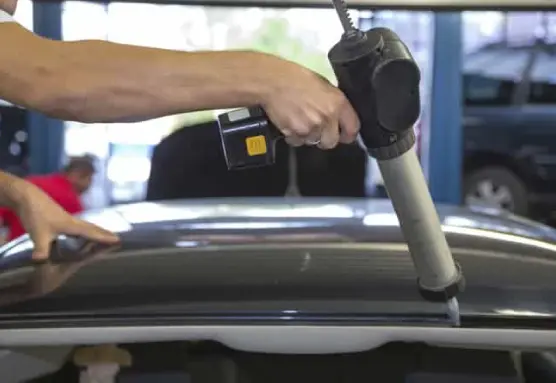 A person using a caulking gun to seal the windshield of the car